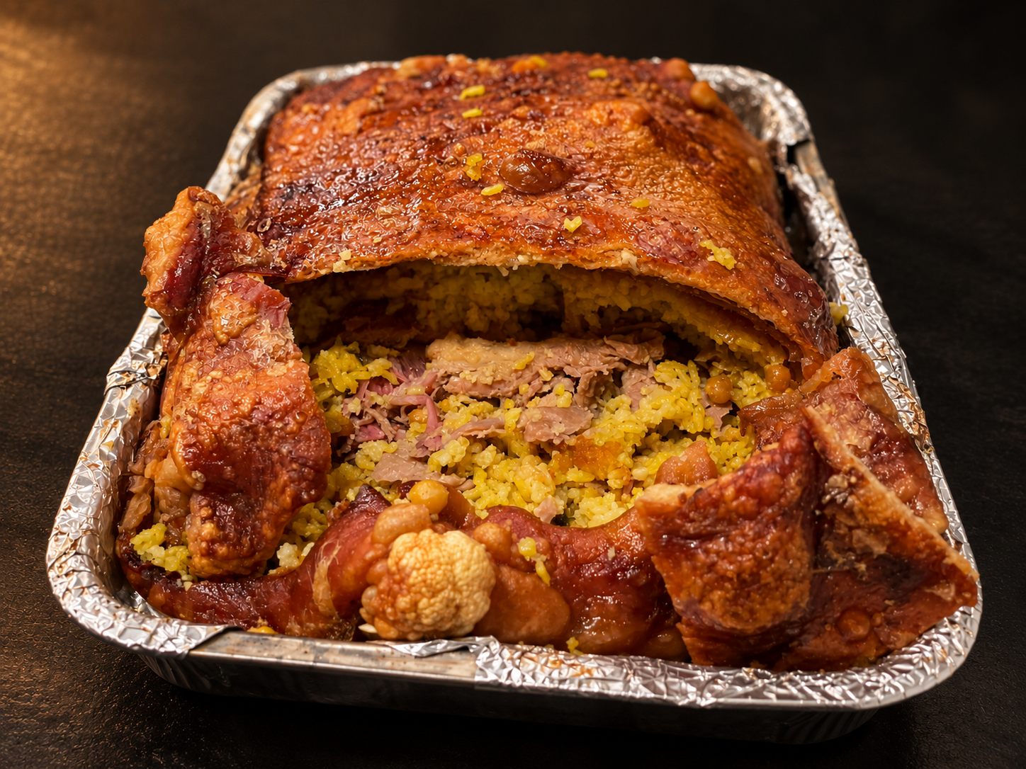 Cojín de lechona colombiana en su bandeja, con la piel dorada y el relleno de arroz y carne a la vista.