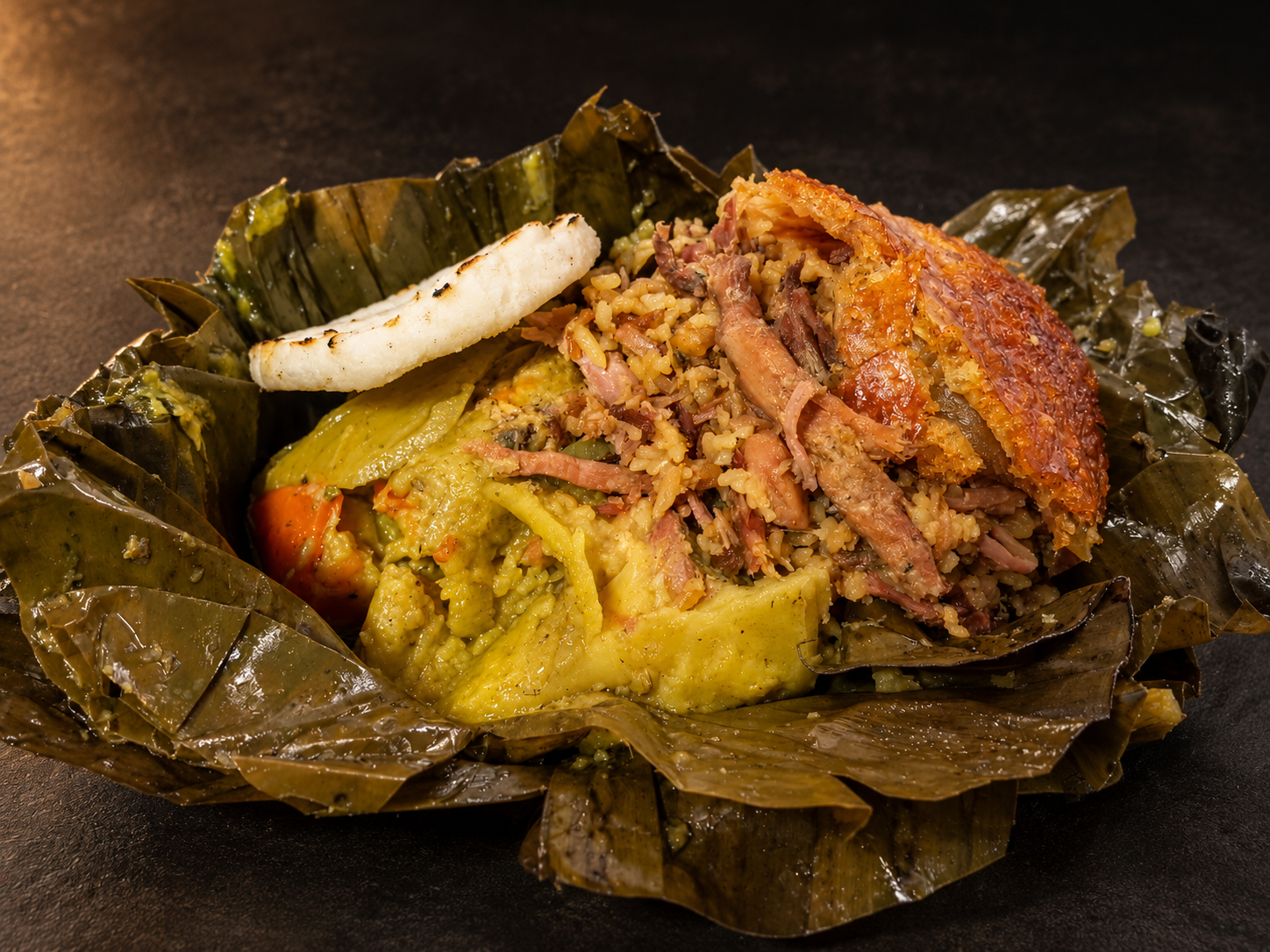 Tamal volteado abierto sobre sus hojas, con lechona y una arepa al lado.